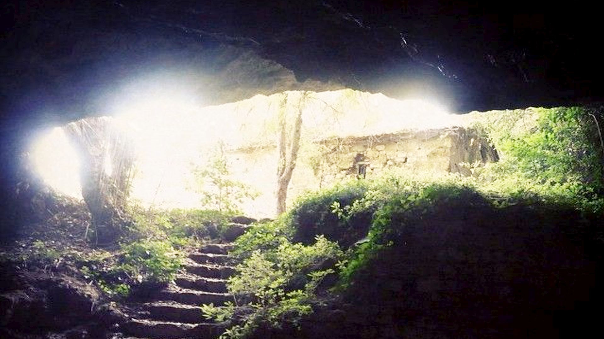 la luce filtra dall'esterno dal grande arco di accesso all'eremo scavato nella roccia. Una scala rustica scende all'interno.
