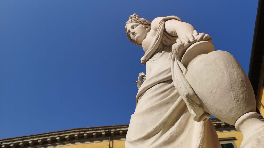 Statua neoclassica della fontana della Naiade, in piazza San Salvatore. Una figura femminile in calcare bianco, con una veste drappeggiata, capelli raccolti e un'anfora.