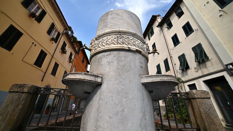 La Fontana di porta san Gervasio a Lucca. Un cilindro di marmo con due vasche in cui versano due zampilli di acqua. Ai lati ci sono le case