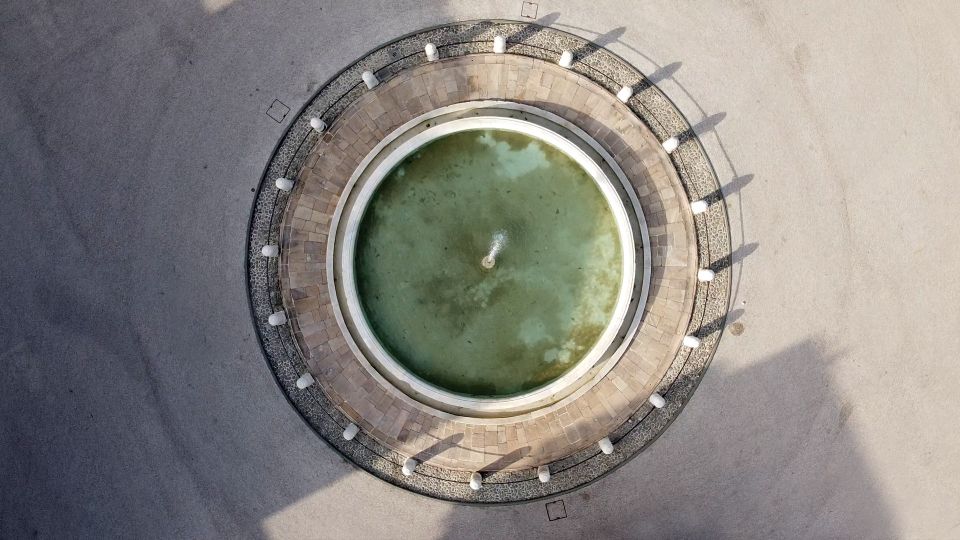 La fontana di piazza Antelminelli a Lucca. Dall'alto ha unaforma perfettamente rotonda con uno zampillo nel mezzo e poi si susseguono un cerchio di marmo, uno di pietra di guamo per la base, 20 pilastrini di marmo collegati con una catena e una canletta di sassi di fiume