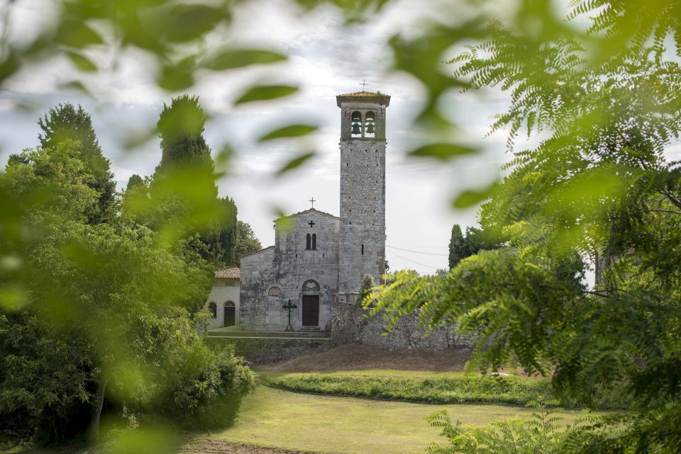 facciata della chiesa di Sant'Andrea di Gattaiola con il campanile attraverso al vegetazione primaverile. La facciata è semplice, a falde con una sola apertura centrale e una finestra a bifora sopra. Sulla sinistra il campanile ha la cella campanaria con una finestra a bifora e due campane.