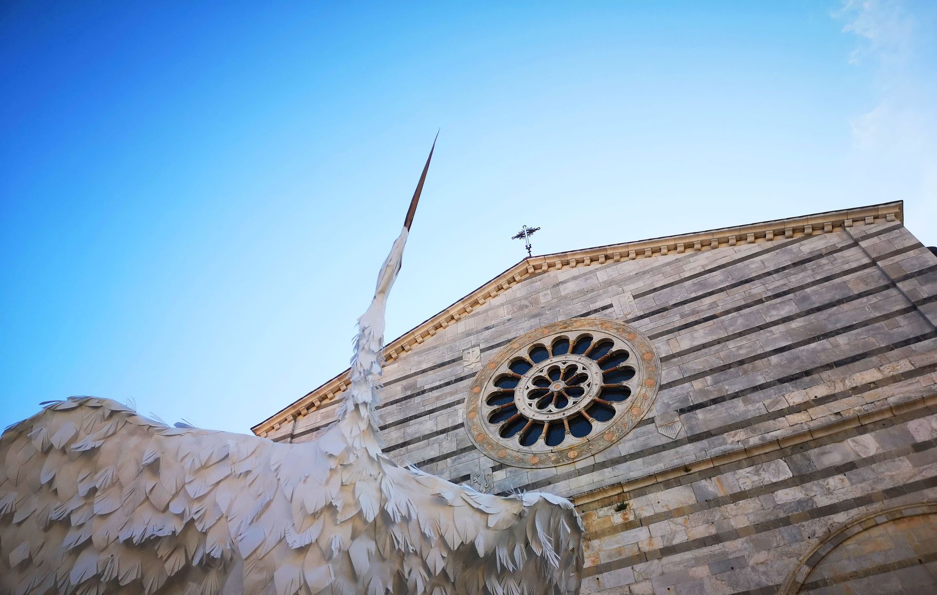 scrorcio in primo piano di una scultura in carta raffigurante un airone con lo sfondo della chiesa di San Francesco
