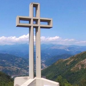 in primo piano una croce monumentale in cemento armato. sullo sfondo montagne