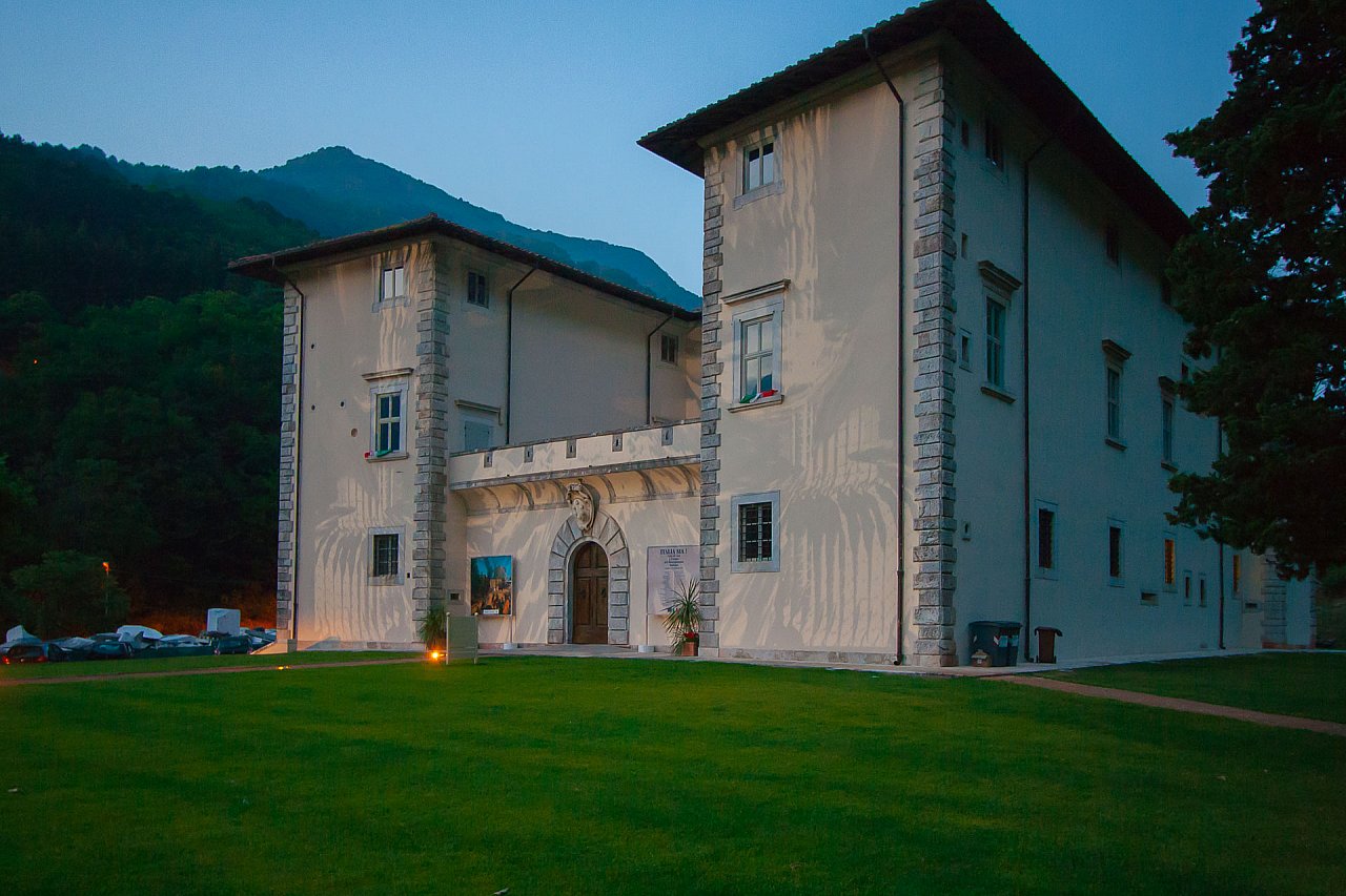 il palazzo mediceo di Seravezza ha due ali laterali di tre piani e un ingresso al centro con un arco in pietra. davanti c'è un prato e sul fondo le Alpi Apuane