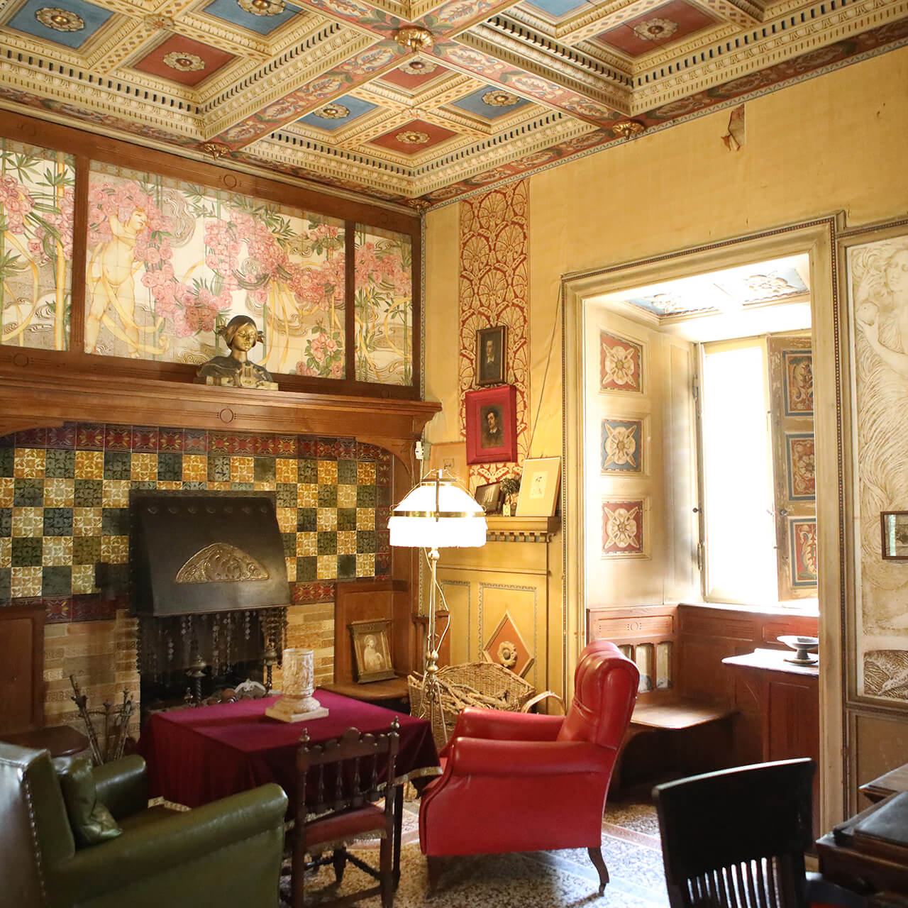 il salotto della Villa Puccini a TOrre del Lago. Una piccola stanza con arredi di gusto liberty, soffitto a cassettoni, un caminetto e una grande finestra.