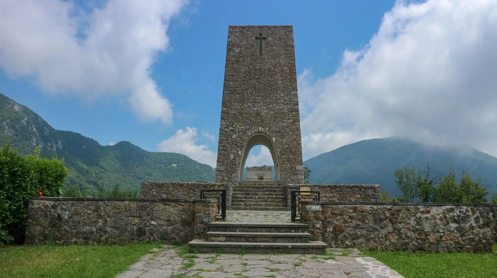 Sacrario delle vittime di Sant'Anna di Stazzema. Un grande arco in pietra che inquadra una tomba. Sullo Sfondo le Alpi Apuane