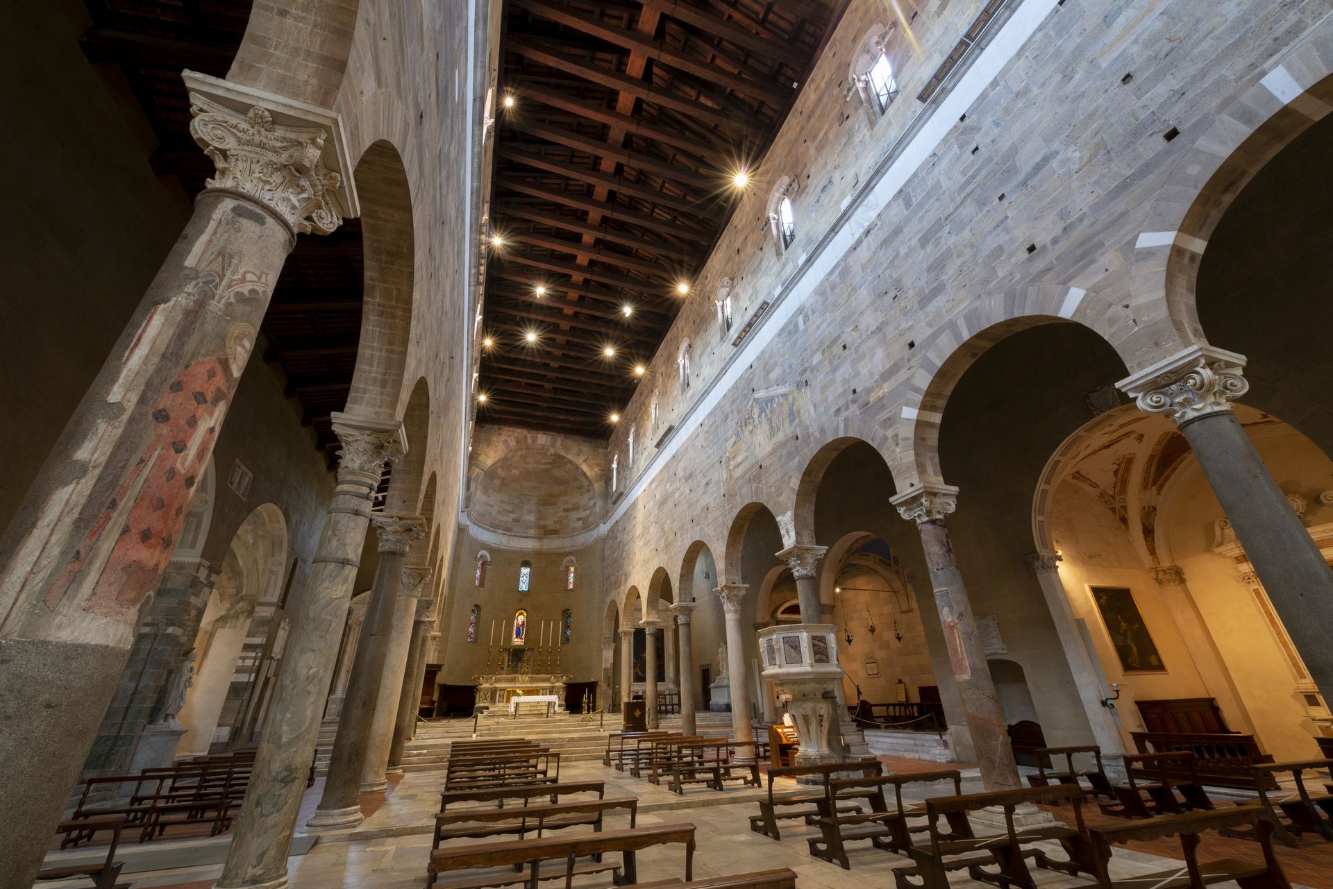 L'interno luminoso e semplice della basilica di San Frediano a Lucca con colonne corinzie e muro liscio. Su alcune colonne, immagini dipinte di santi. Il soffitto è a capriate in legno