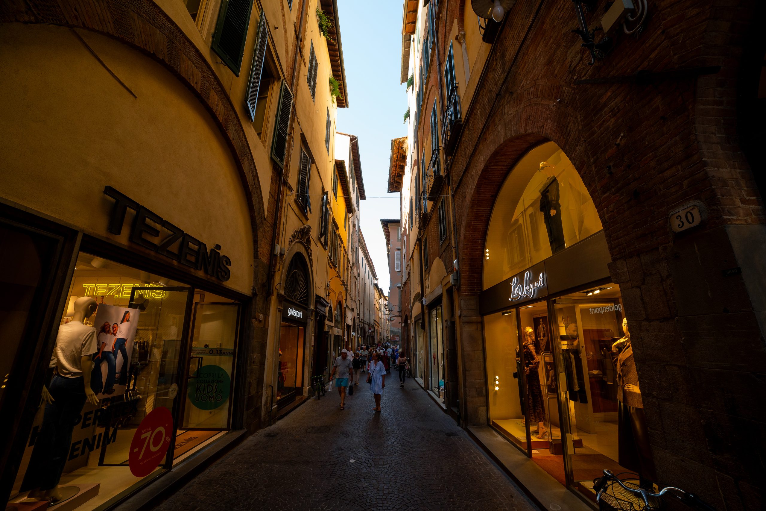Scorcio di via Fillungo con vetrine di negozi illuminate e persone che passeggiano