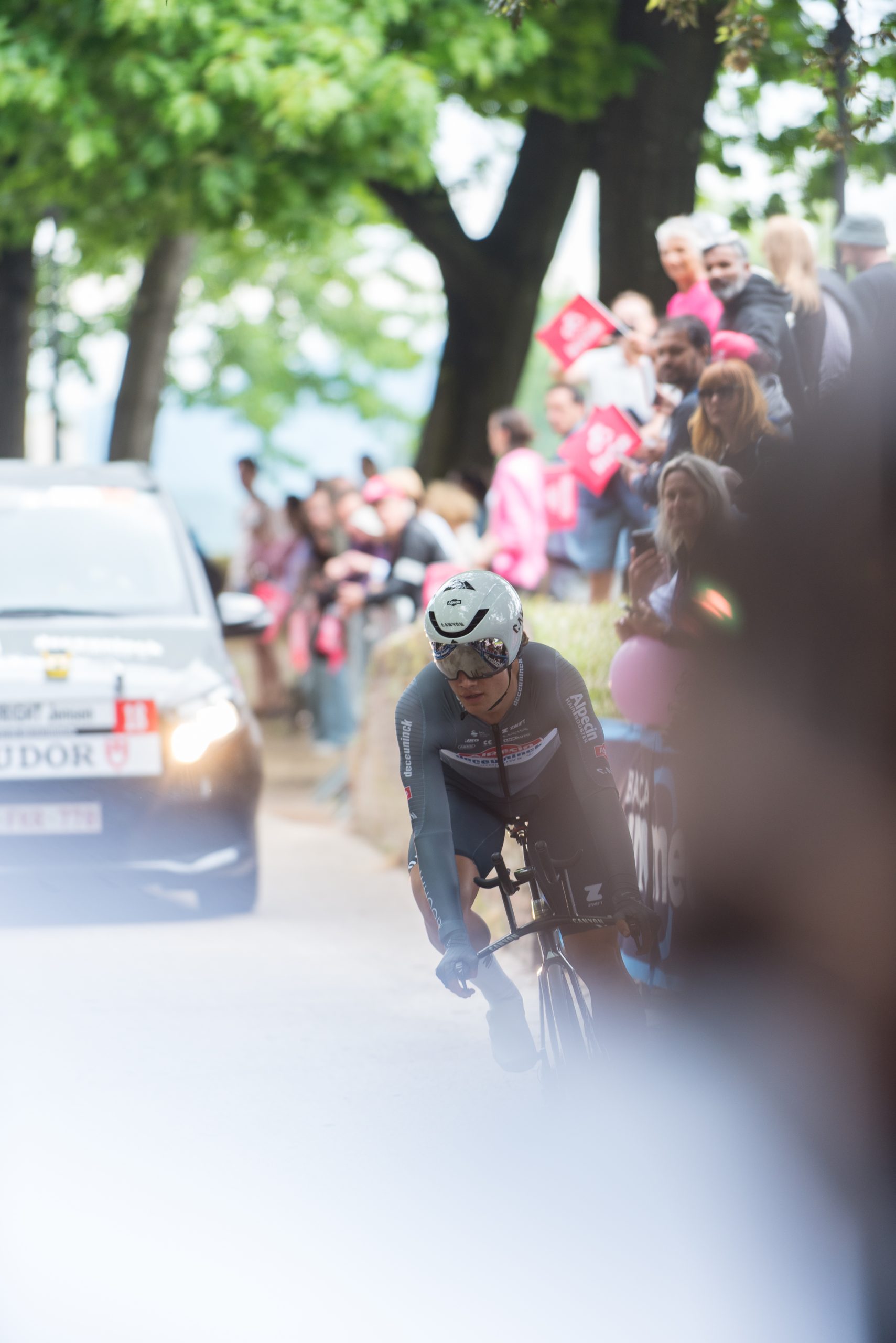 Folla sulle Mura di Lucca al passaggio del Giro d'Italia. in primo piano un ciclista e sullo sfondo, fuori fuoco, persone con bandierine sotto gli alberi delle Mura.