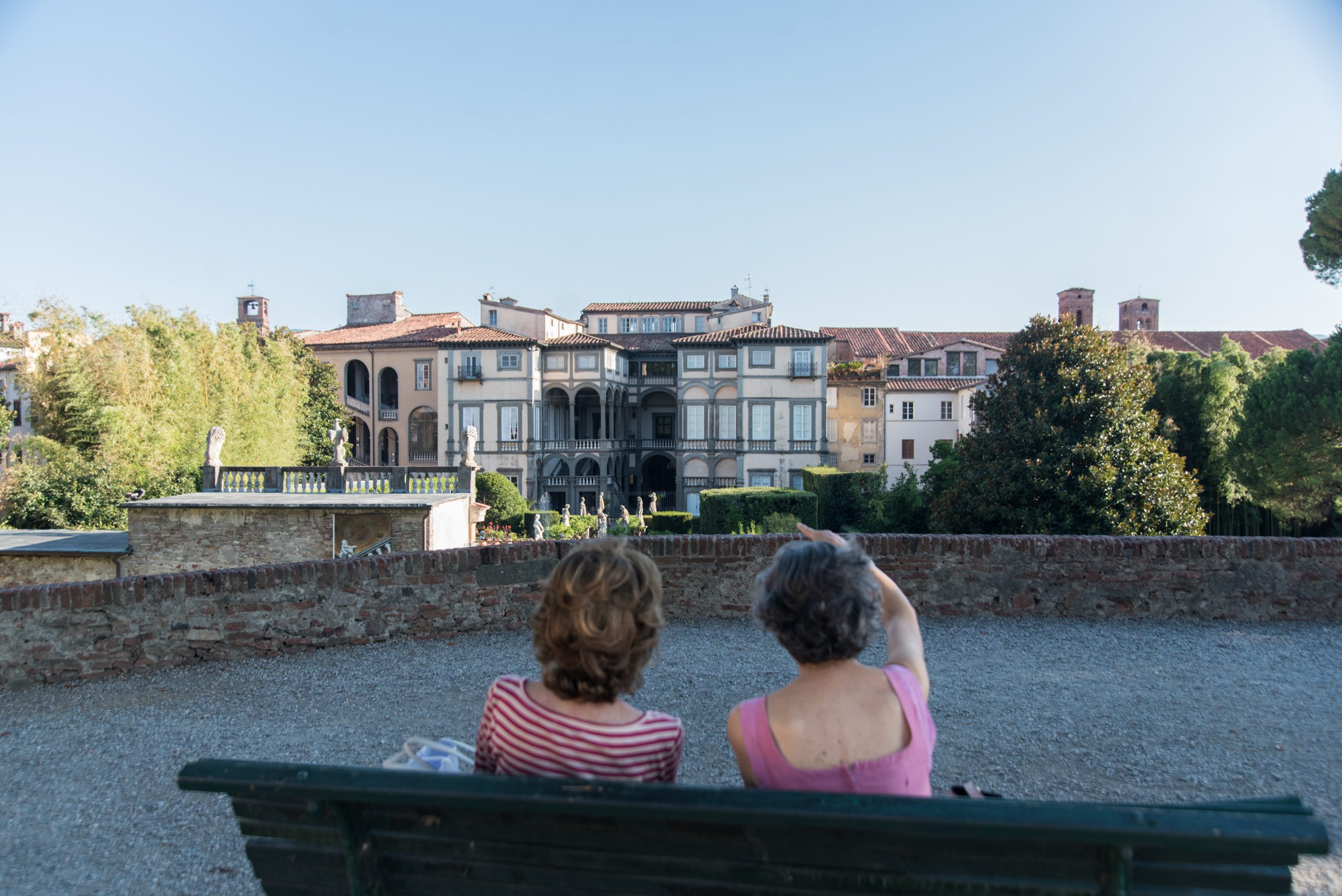 Due donne guardano Palazzo Pfanner sedute su una panchia delle Mura di Lucca.