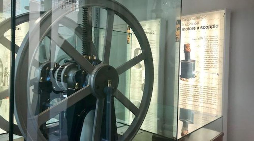 Interno del Museo del Motore a Scoppio. In primo piano gli ingranaggi di un motore e sulla parete pannelli esplicativi