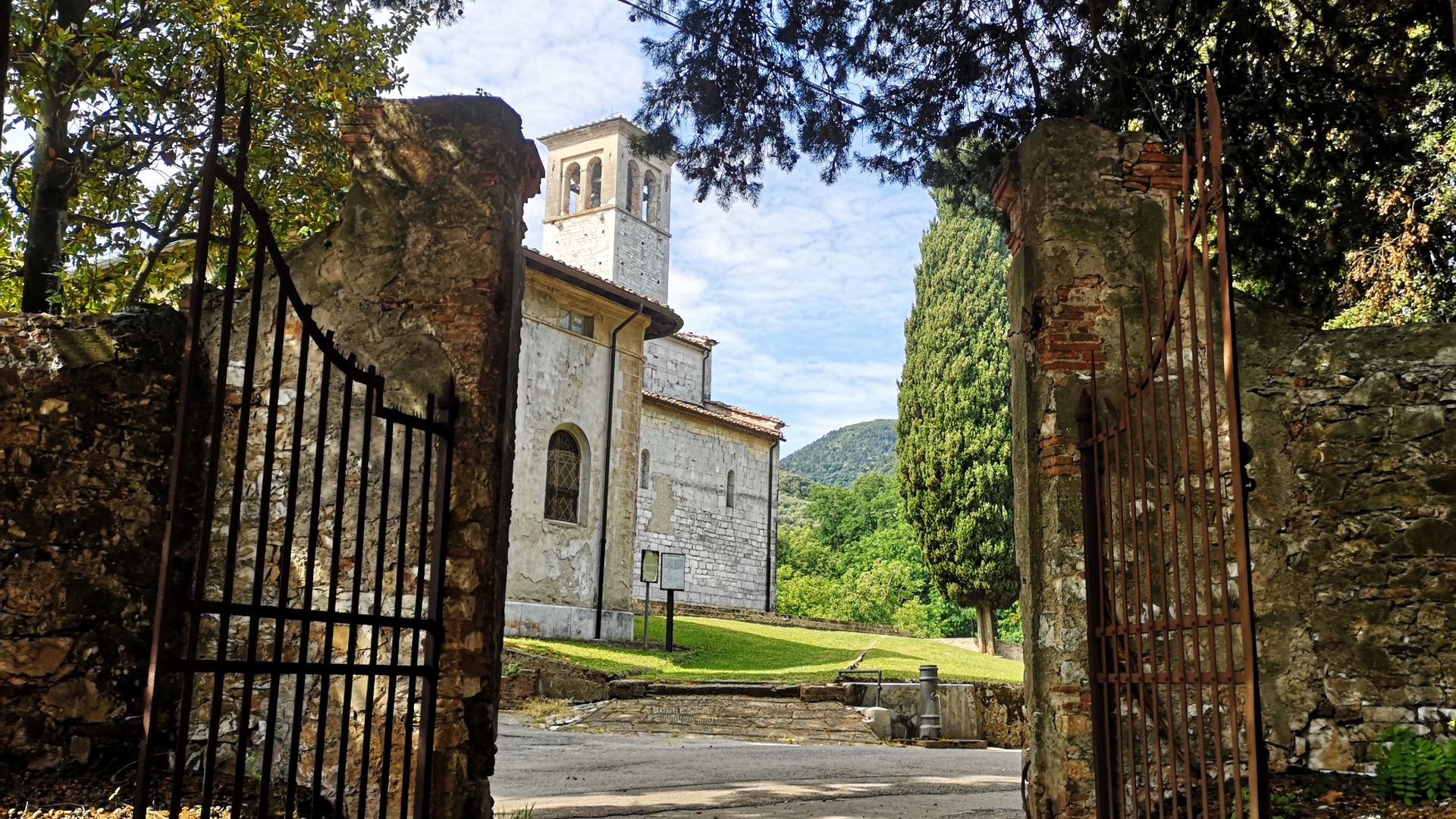 Oltre il cancello che si apre in un muro di campagna, c'è la pieve romanica di Sant'Andrea di Gattaiola con il campanile. Accanto alla pieve c'è un cipresso e tutto intorno un prato