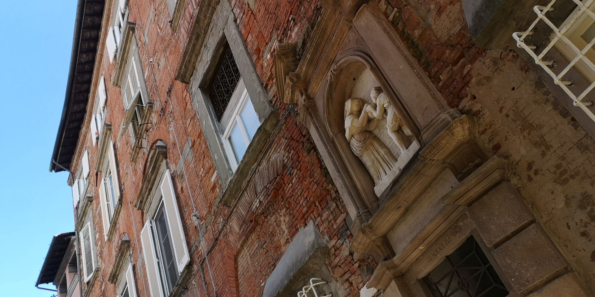 facciata del palazzo Fatinelli. Un edificio in mattoni facciavista con grandi finestre dalle cornici in pietra serena. In un anfgolo un bassorilievo descrive Santa Zita che offre acqua a un pellegrino. Sotto il bassorilievo la portella del pozzo.