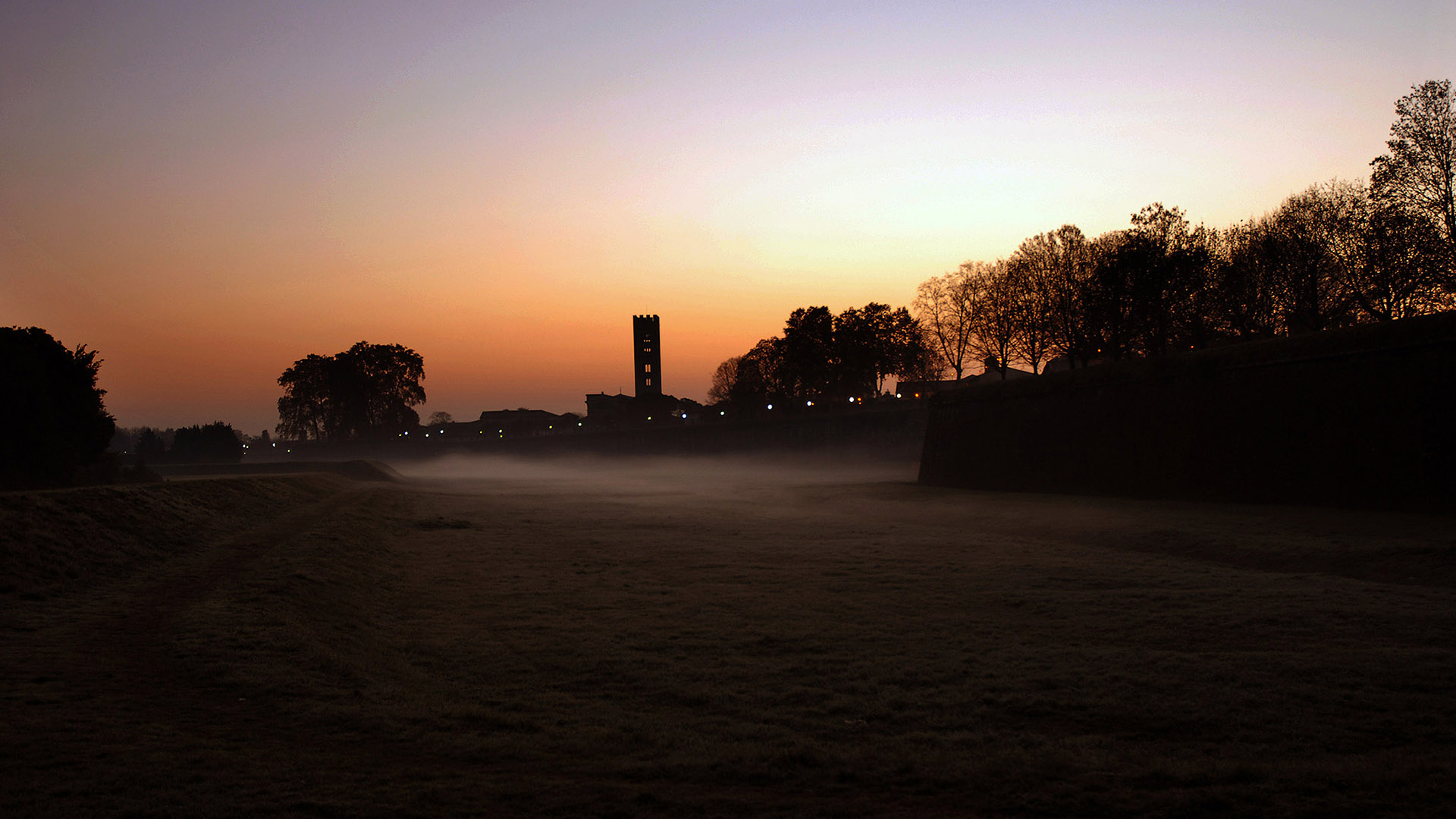 il profilo delle Mura di Lucca con il campanile di san Frediano nei colori di una mattina di nebbia