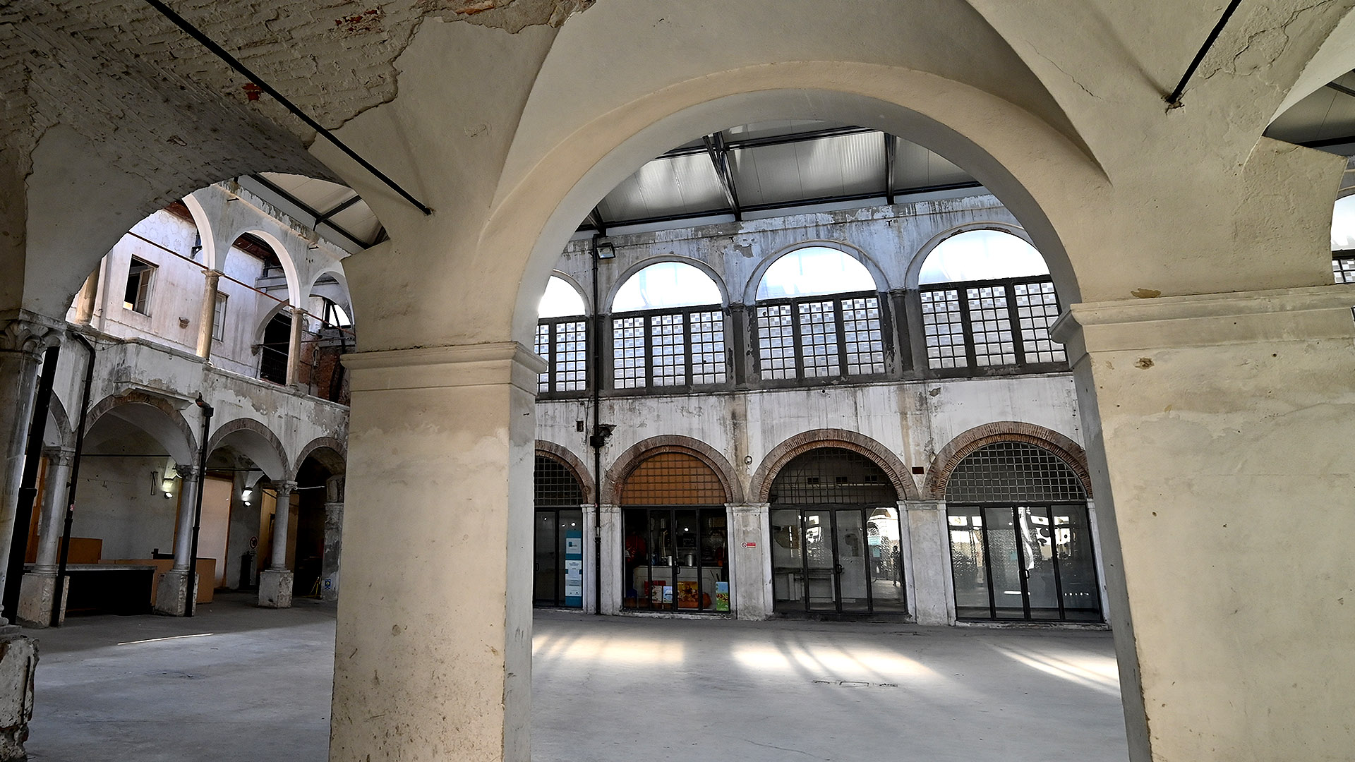 interno del Mercato del Carmine dal percorso sotto il loggiato. Oltre l'arco c'è il chiostro con percosi aperti nella aprte inferiore e chiosi con vetrocamera nella parte superiore