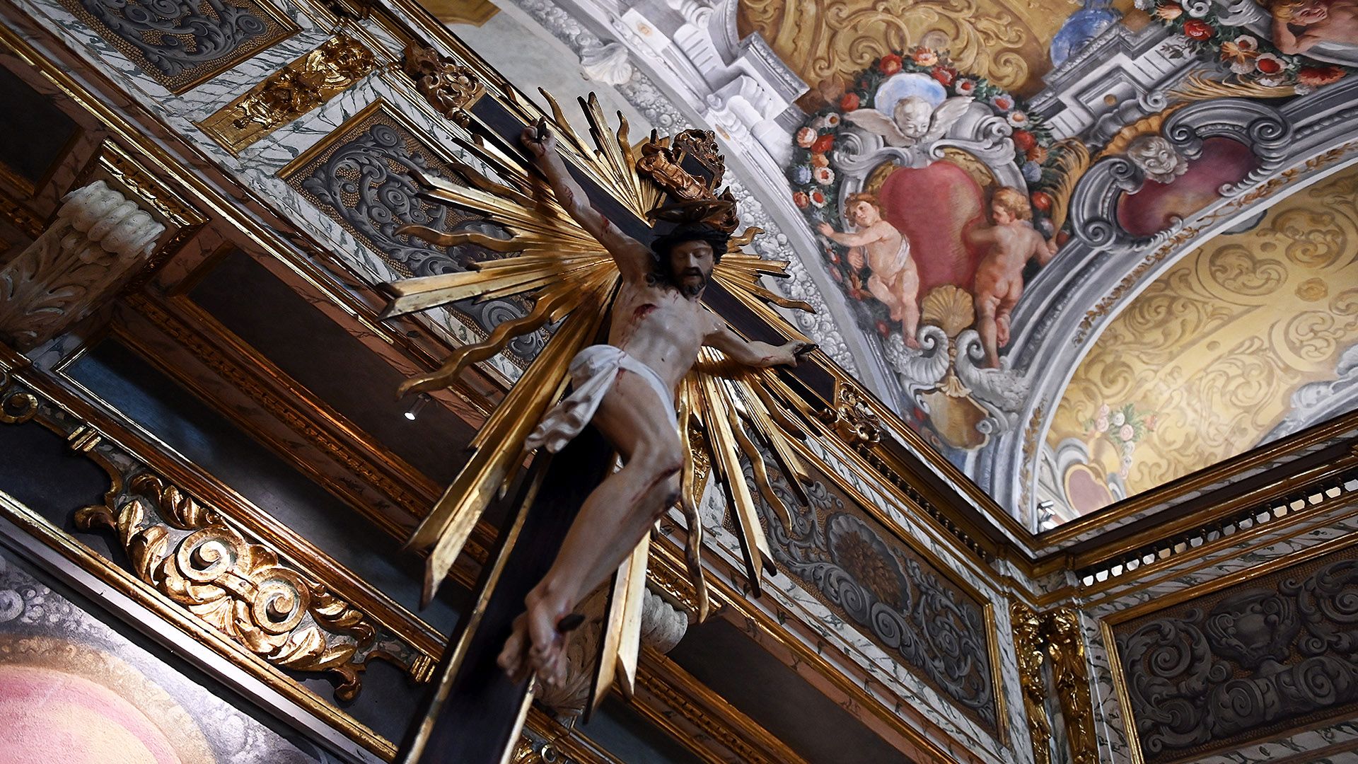 Crocifisso con decorazione barocca della luce dello spirito Santo nell'oratorio degli angeli custodi. Le pareti sono decorate con effetto trompe loieil di decorazioni a bassorilievo dorate e marmi, putti che reggono festoni di fiori e architetture.