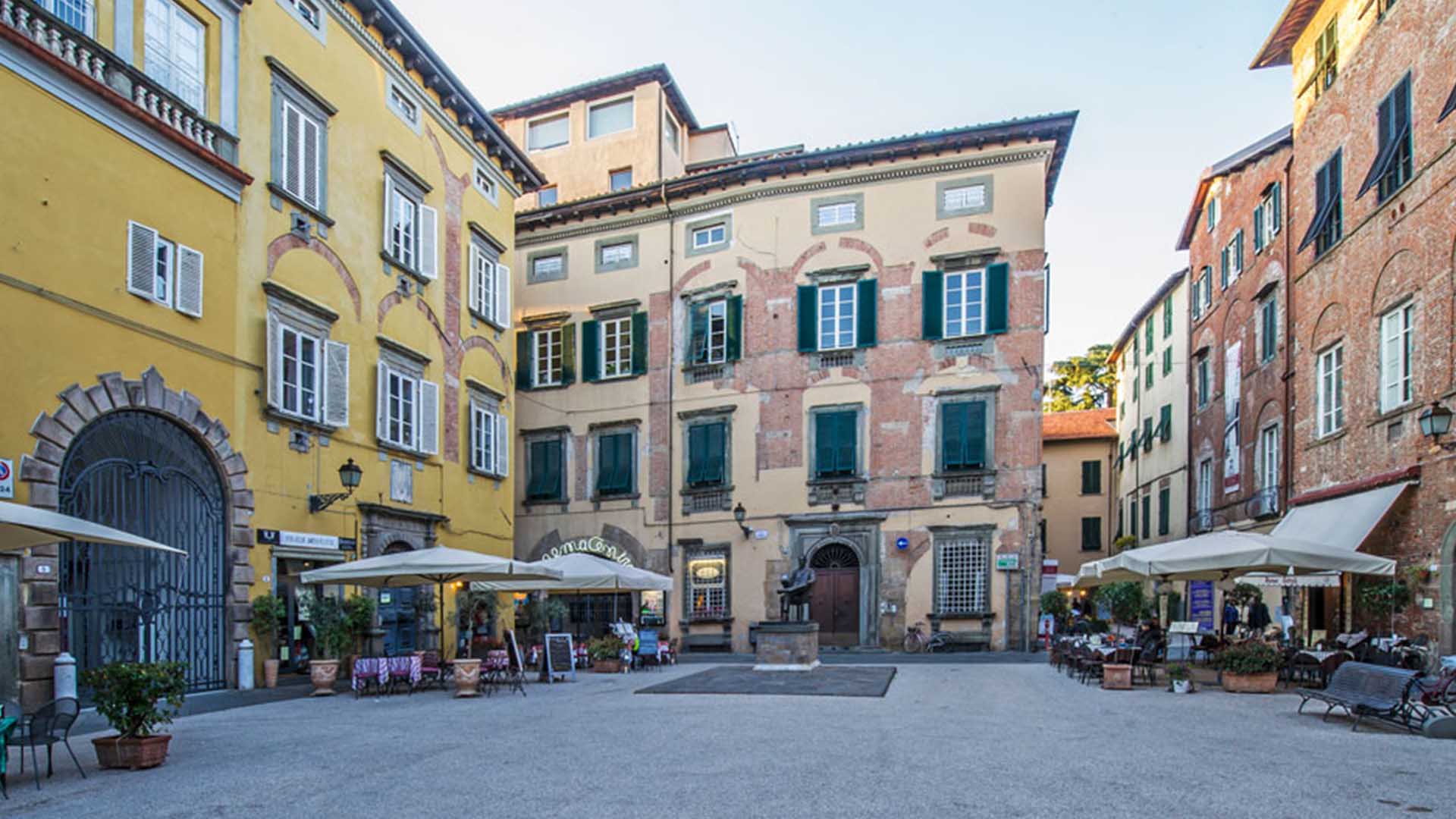 Piazza Citatdella con la statua di Giacomo Puccini e le tende di alcuni bar ai lati