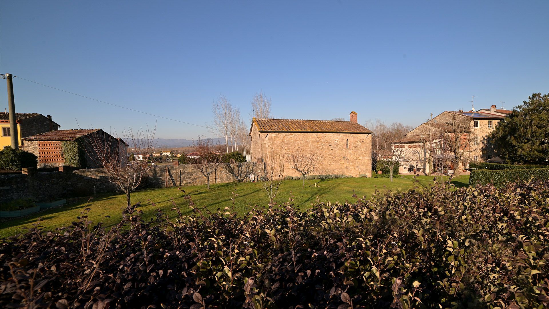 Oltre una siepe e un campo c'è la piccola pieve e oratorio di San Quirico in Casale n mezzo alle case del borgo di San Quirico.