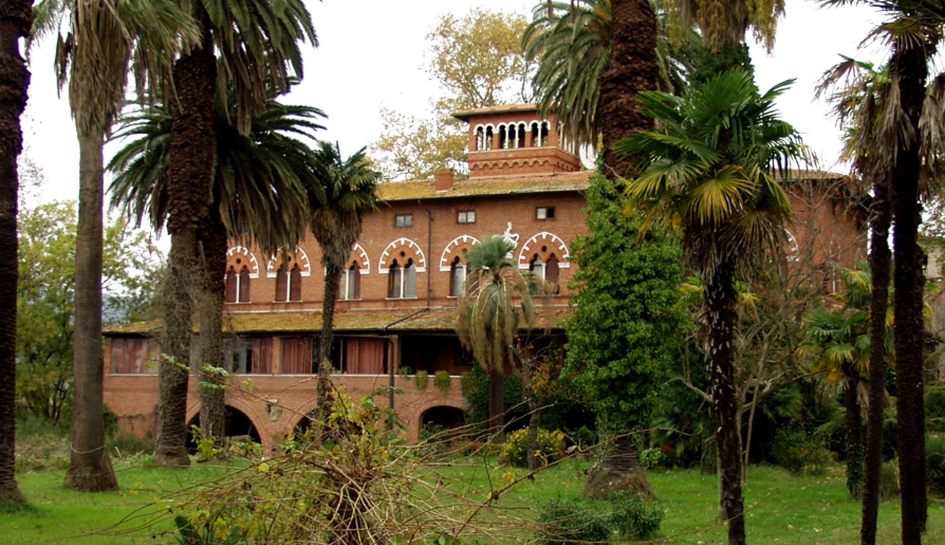 Villa Ginori Lisci a Massaciuccoli, nel parco di palme e altre iante acquatiche. La costruzione è in stile neogotico, in mattoni rossi con finestre a bifora e decorazioni in marmo bianco