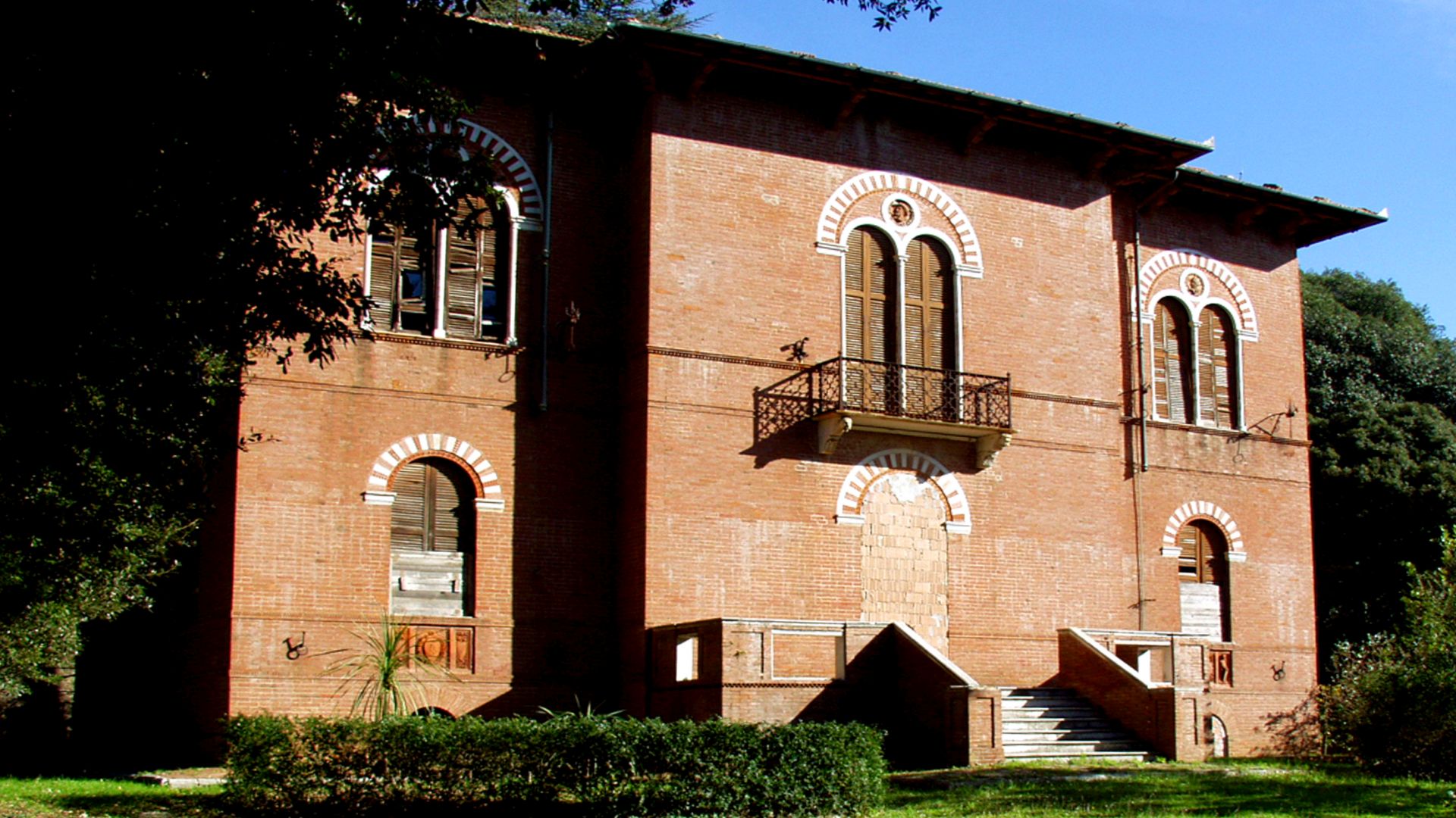 facciata della Villa Puccini di Chiatri in stile neorinascimentale circondata dal giardino. E' costruita in mattoni rossi con finestre a bifora con colonnine bianche e decorazioni sull'arco in mattoni e marmo bianco. Il villino è a due piano e si accede da una scala esterna con terrazzino