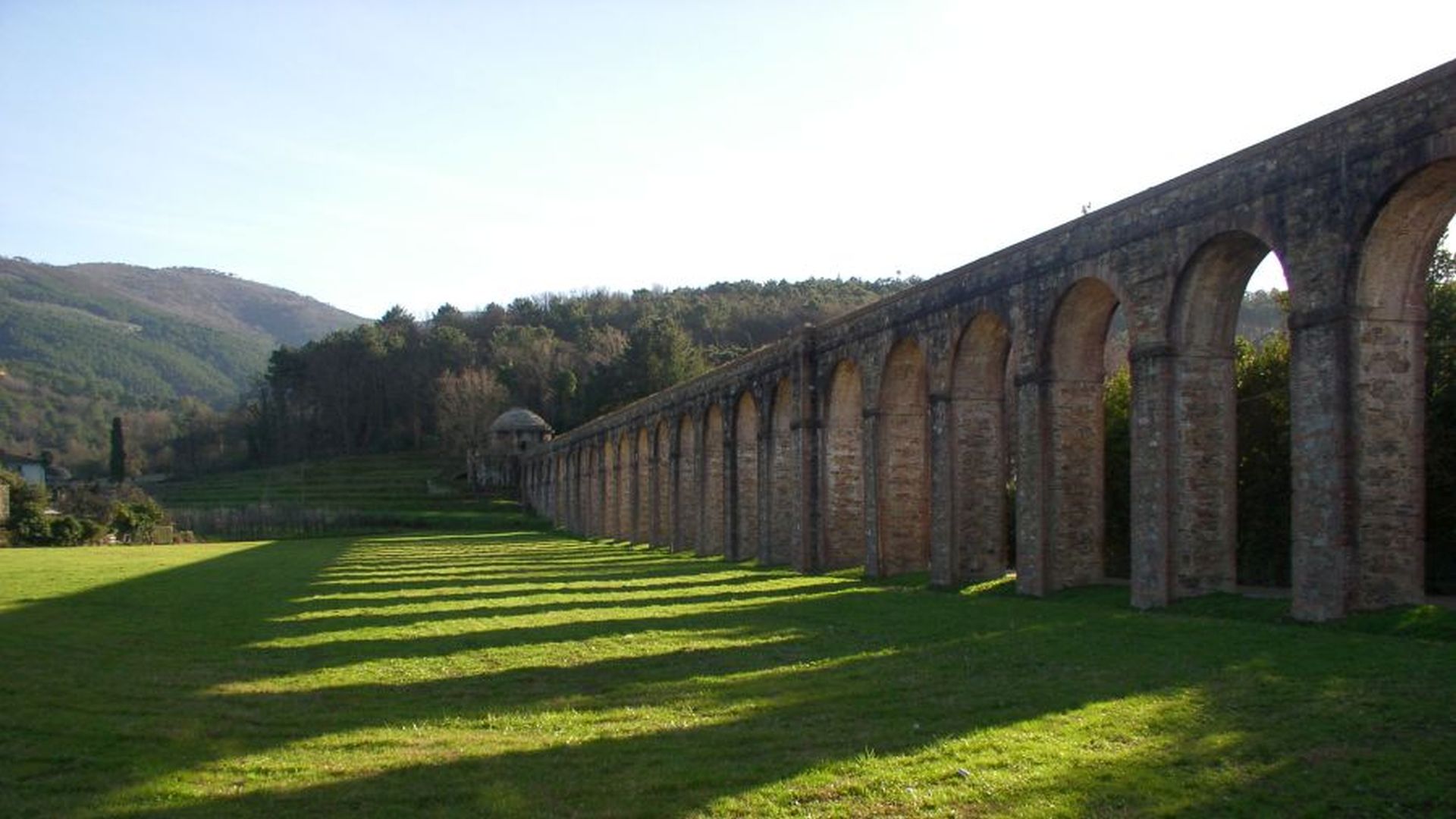 Le arcarte dell'Acquedotto del Nottolini terminano con il tempietto di monte. Intorno ci sono dei prati e sullo sfondo le colline del Monte Pisano