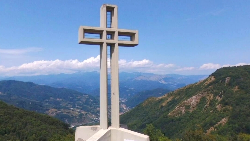 la croce di Brancoli di fronte al paesaggio della Valle del Serrchio e dell'Appennino. Il cielo è limpido, con nuvole.
