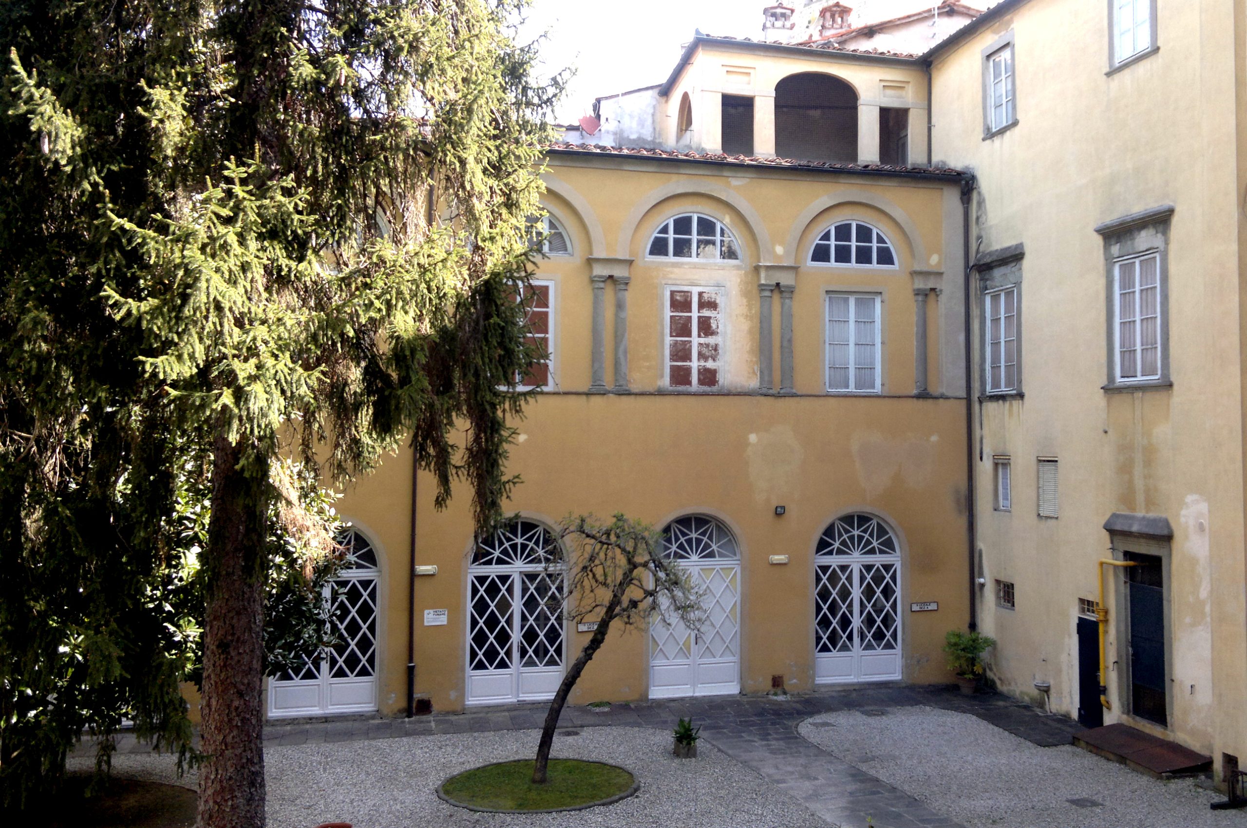 Cortile del palazzo Lucchesini tra due edifici ad angolo. La facciata sulla destra ha una porta a piano terra e due finestre al piano superiore. L'edificio sul fronte ha quattro porte con decorazioni al piano terra e una serie di archi ciechi con doppia colonna e all'interno finestre. sopre c'è una loggia a serliana.