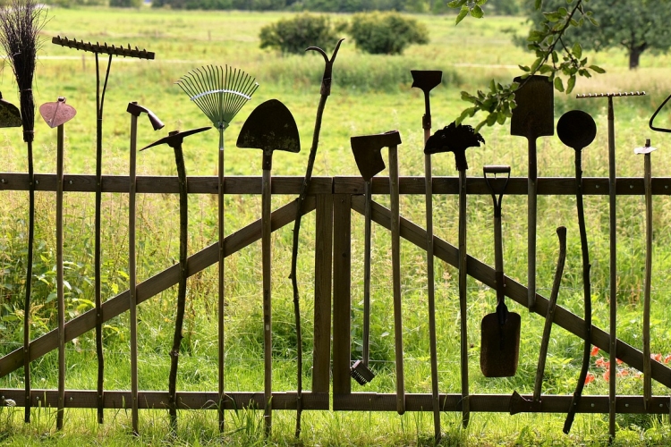 un cancello in legno in un prato con attrezzi da lavoro agricoli appesi verticalmente