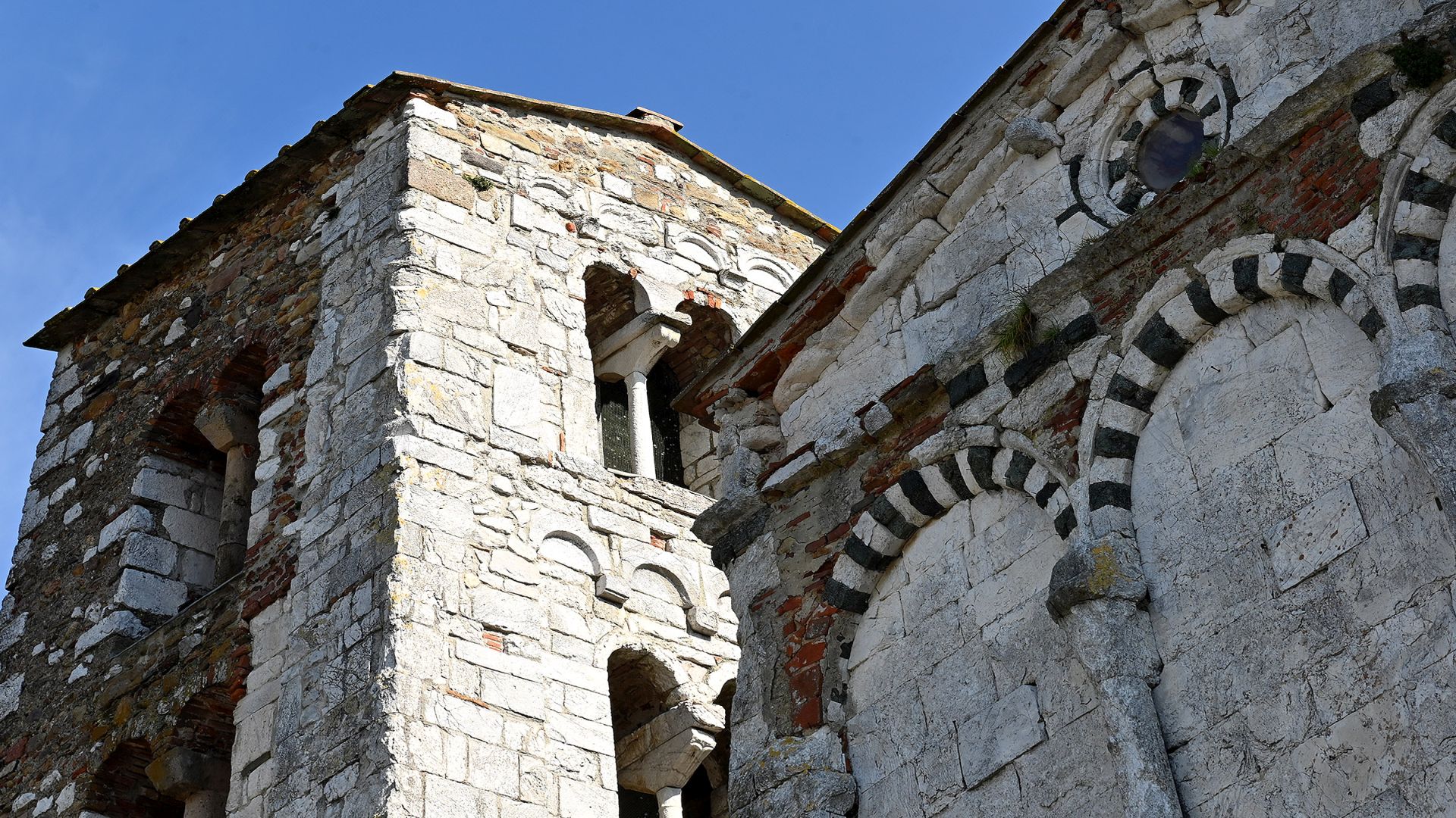 il campanile in pietra con bifore e la parte alta della facciata della pieve di San Giovanni Battista (pieve vecchia) a Santa Maria del GIudice con archi ciechi decorati in calcare bianco e verde