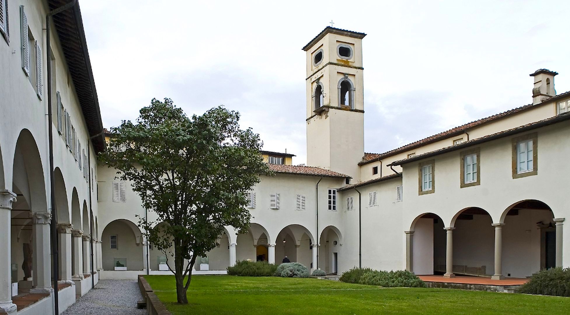 chiostro del complesso di San Micheletto con campanile. Al centro aiuole con prato, cespugli di erbe aromatiche e un albero. Intorno l'edificio con i loggiati al piano inferiore e al piano superiore finestre rettangolari