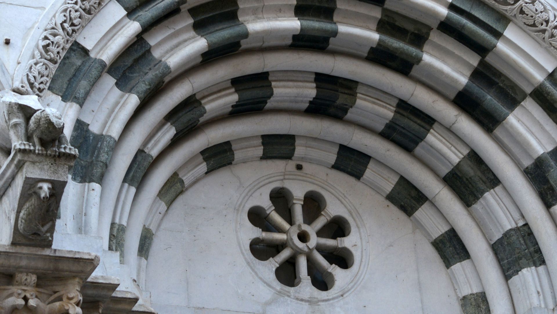 Particolare della strombatura della porta principale a fasce di marmo bicolore della chiesa di San Cristoforo. L'arco più eterno decorato con motivi floreali e la mensola su cui poggia con la figura di una pecora