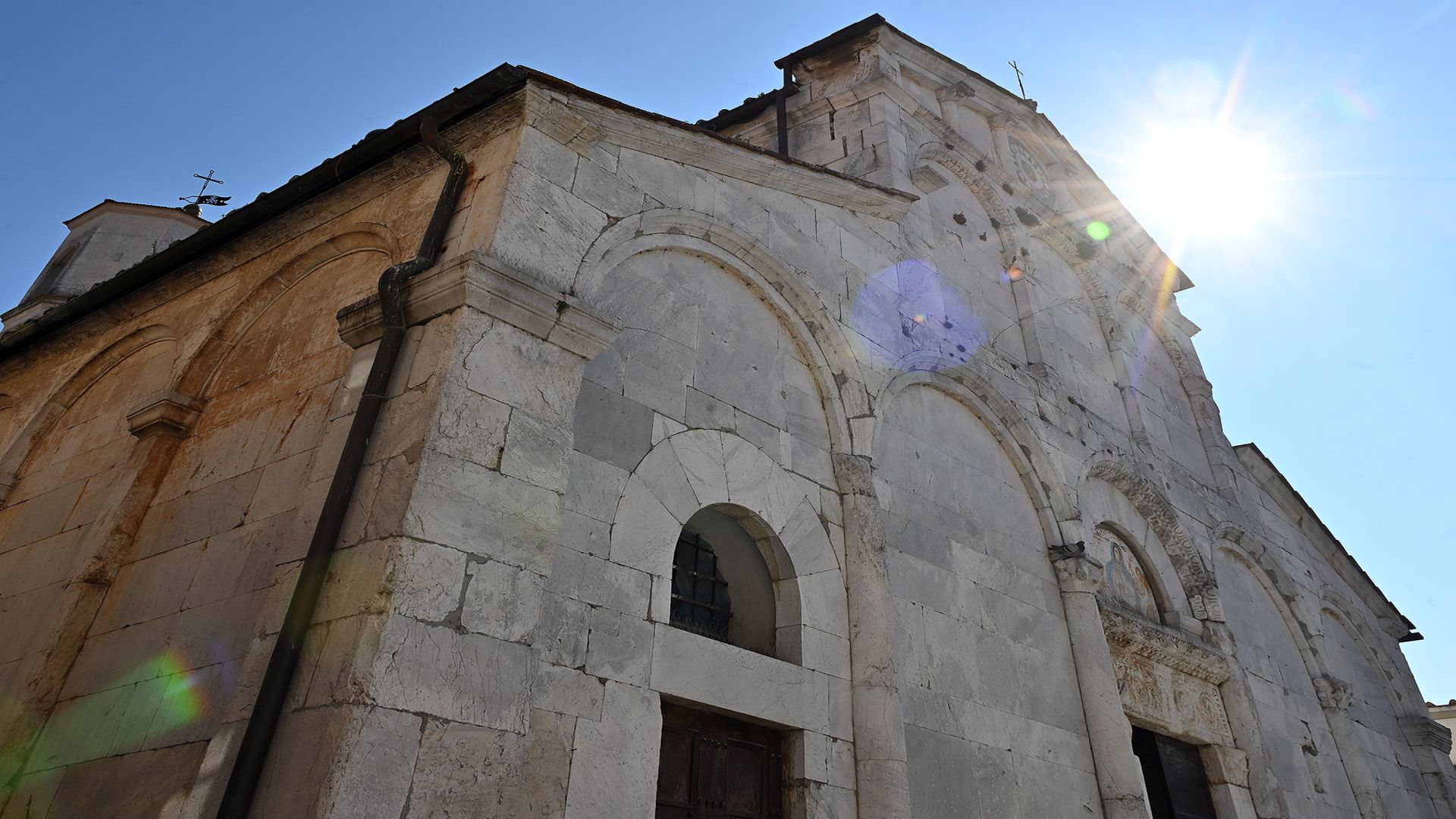 Un raggio di sole illumina la pieve nuova di Santa Maria del Giudice. La chiesa in marmo bianco ha 5 arcate cieche alla base. nelle dispari si aprono le porte di accesso alla chiesa. Nella parte superiore due ordini di arcatelle cieche e un piccolo rosone