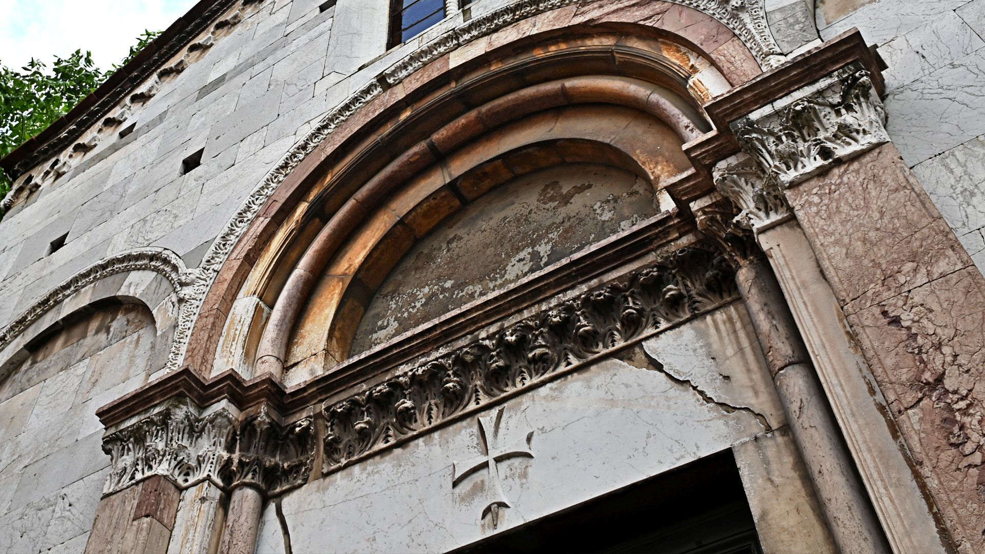 Particolare dell'arco strombato e dell'architrave della chiesa di Santa Giulia su cui è scolpita una croce di malta. L'arco è fatto in marmi di diversi colori.