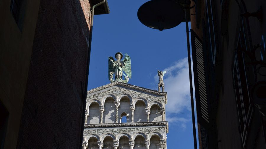 tra due eddifici in ombra si staglia l'angelo San Michele in cima alla facciata della chiesa, In mano ha i simboli del regno e ai suoi piedi un drago sconfitto. Al suo fianco un angelo che suona l'olifante.