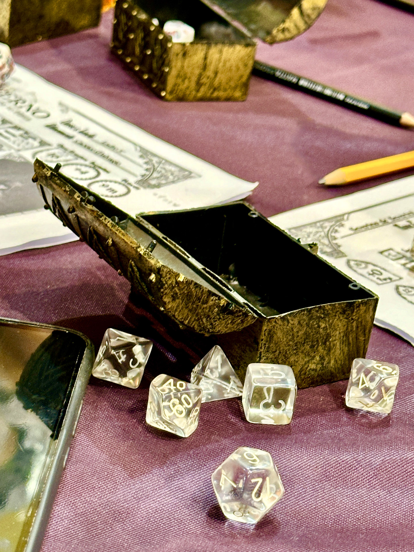 Un piccolo scrigno da pirata, dadi da gioco, matite e mappe su un tavolo da gioco.