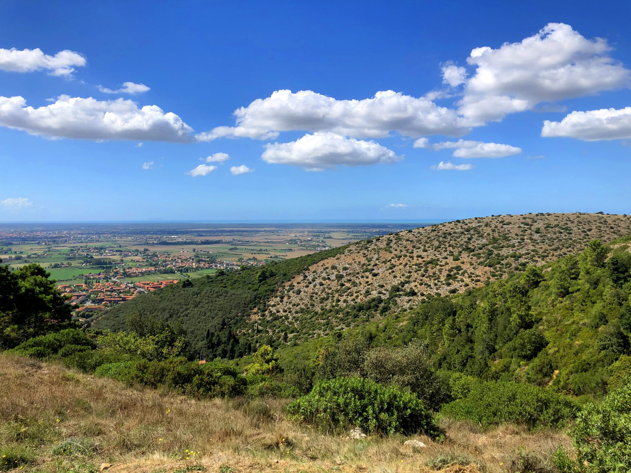 Panorama primaverile da un versante brullo del Monte Pisano sulla Piana di Pisa e, in lontantanza, il mare. Nel cielo ci sono nuvole bianche