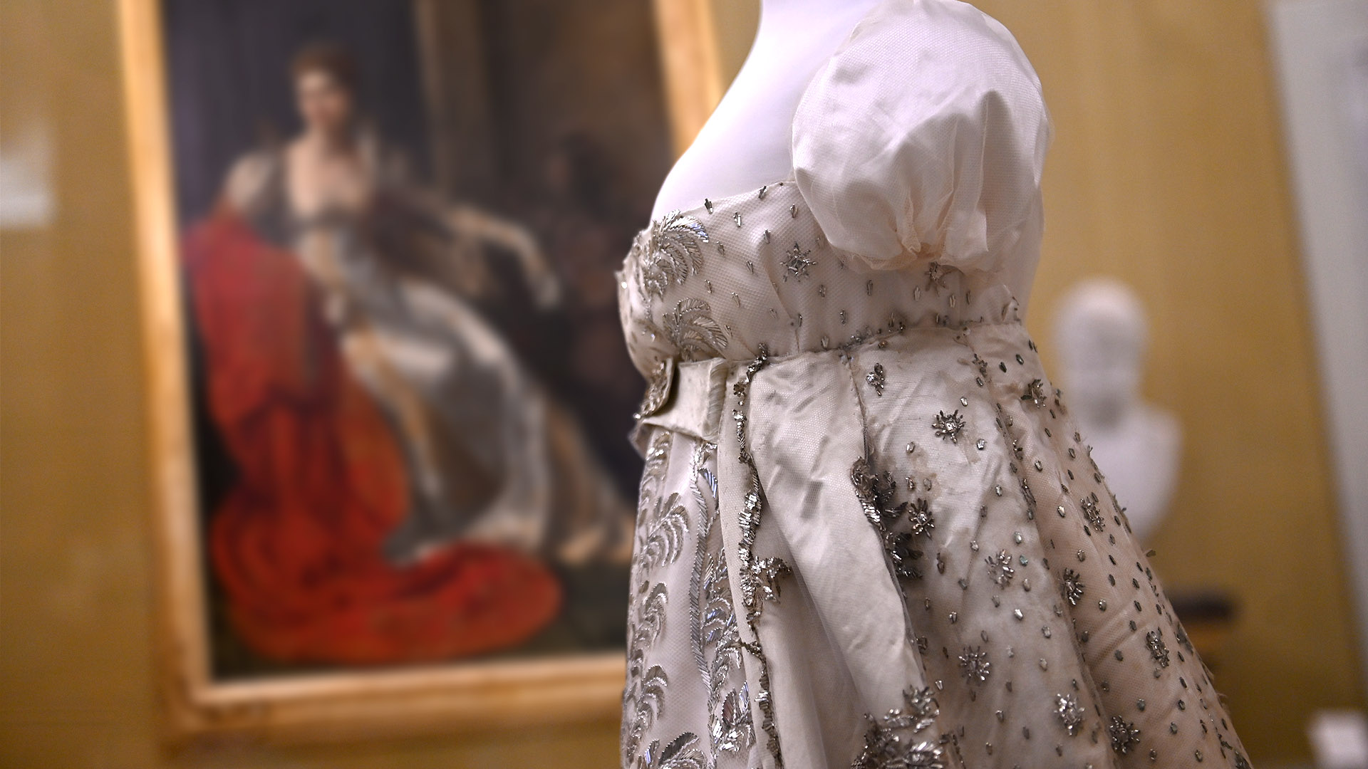 L'abito della corte napoleonica in seta e ricami d'argento custodito al Museo Nazionale di Palazzo mansi. Sulla parete di fondo c'è il ritratto di Elisa Bonaparte in trono che indossa un abito simile