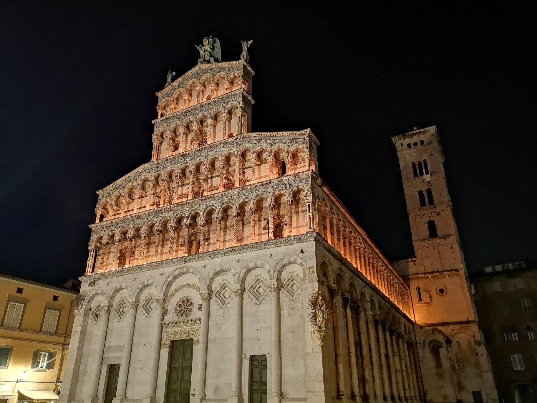 Chiesa di San Michele di notte, illuminata con candele per la processione di Santa Croce. La chiesa ha una decorazione con arcate cieche nella parte più bassa per tutto il perimetro e 4 loggette nella parte superiore della facciata a vela. IN cima alla faccaita la statua di San Michele arcangelo. Su uno spigolo della chiesa un altare pensile con la vergine con bambino