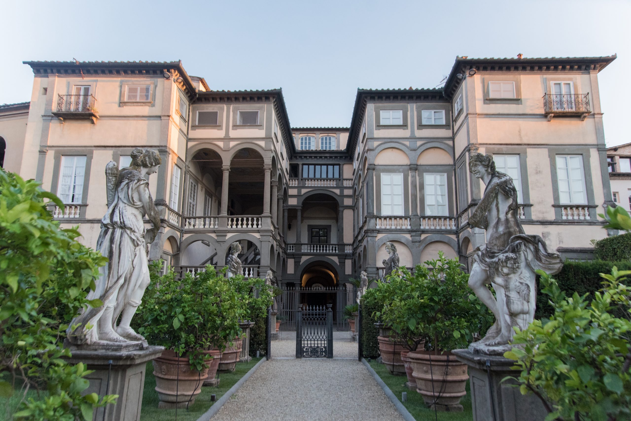 Facciita del Palazzo Pfanner vista dal giardino. In primo piano di cono due statue di ninfe e file di limoni che arrivano fino a un piccolo cancello. Oltre questo sta il palazzo in stile neoclassico con colonnati, atrio e scalone