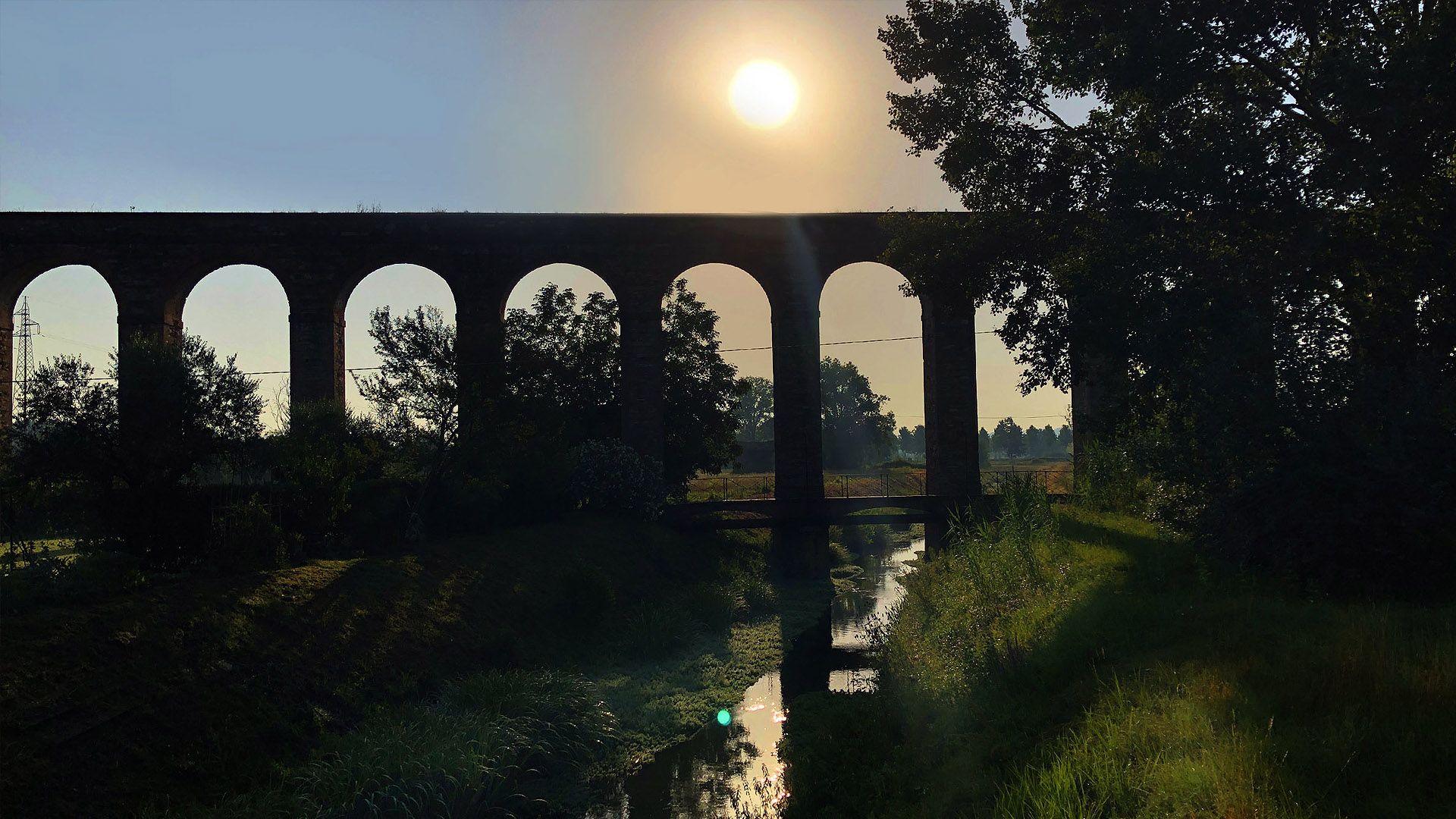 Il sole al tramonto disegna le arcate dell'acquedotto del Nottolini tra gli alberi e si riflette nel torente che passa sotto gli archi