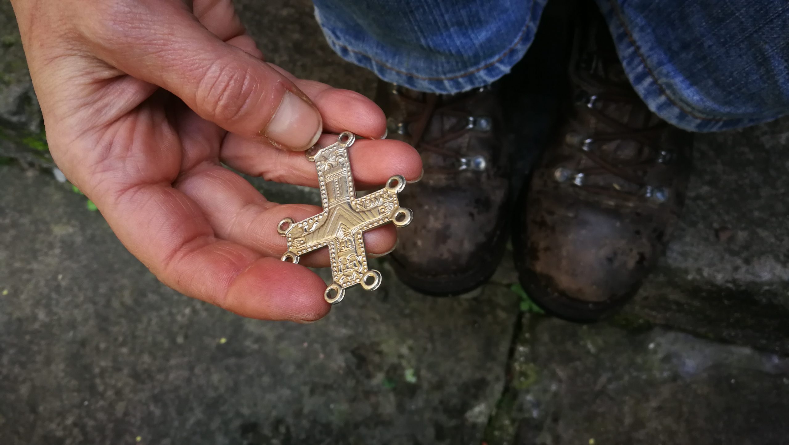 Una mano regge il simbolo dei Pellegrini francigeni di Lucca. Una piccola croce con il Volto Santo da cucire al mantello