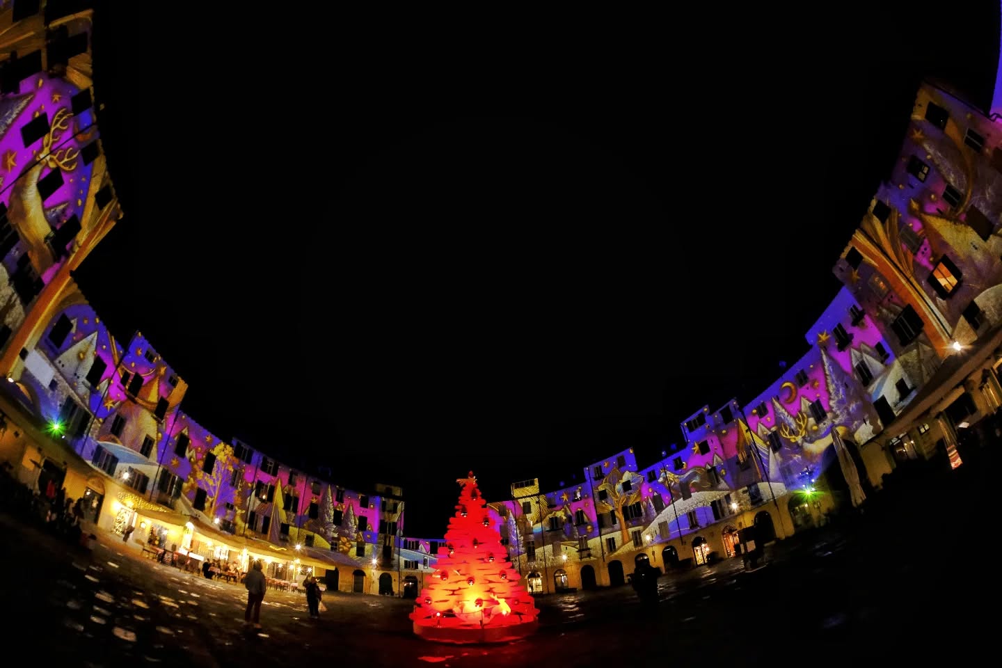 piazza dell'anfiteatro illuminata con proiezioni natalizie e una lbero di natale rosso al centro
