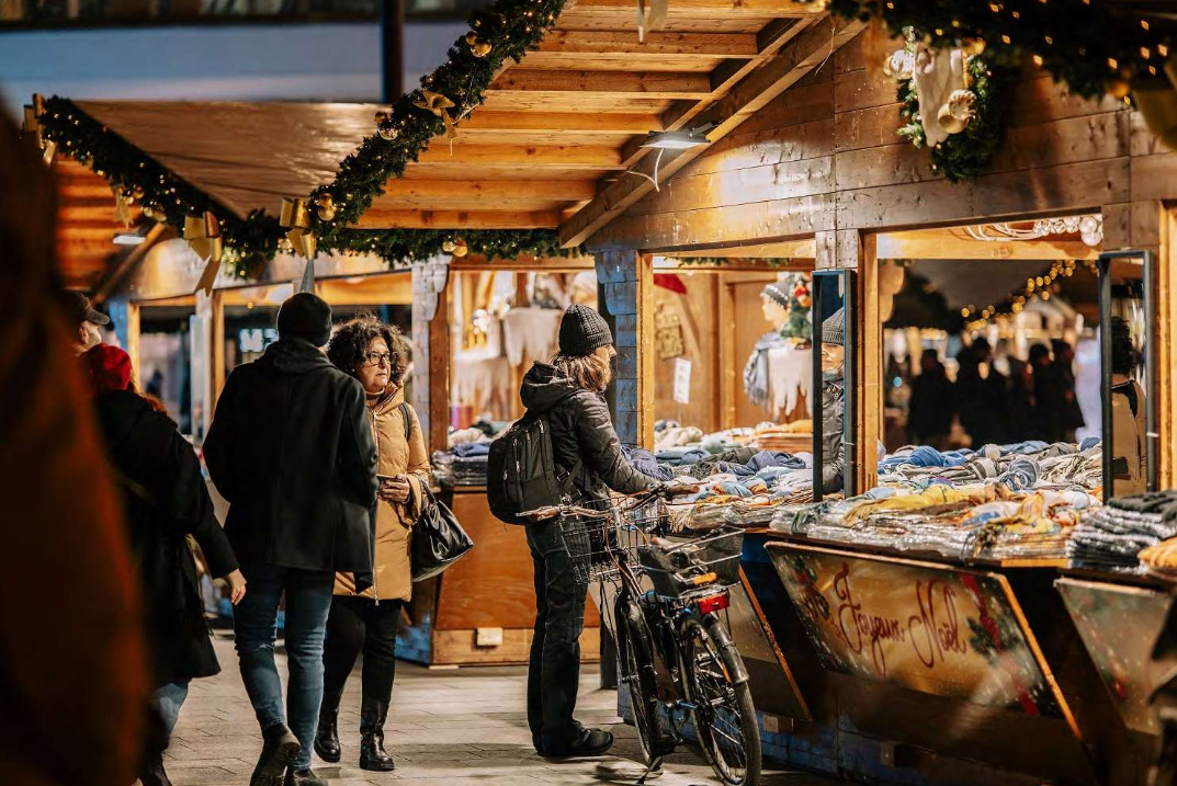 alcune persone tra le casette in legno illuminate di un mercatino di natale