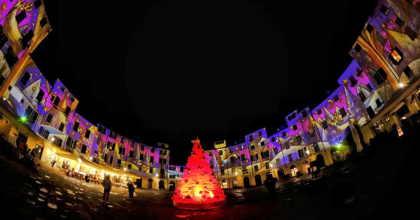 piazza dell'anfiteatro con le proiezioni natalizie sulle facciate e un albero di natale rosso stilizzato al centro