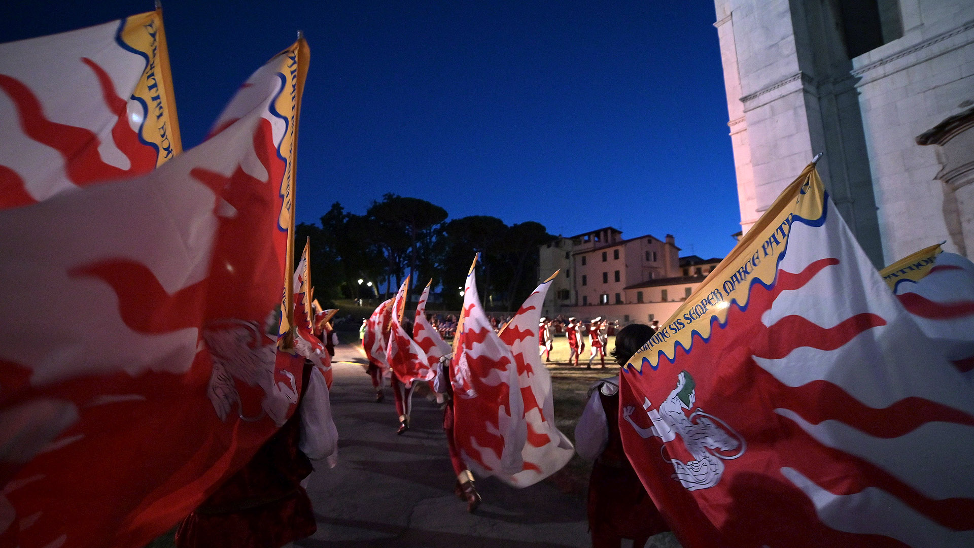 un gruppo di sbandieratori in notturna dietro al cattedrale