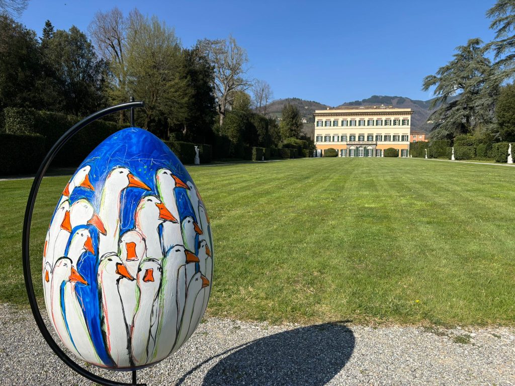 panorama di villa reale tra la vegetazione. in primo piano un uovo di pasqua gigante decorato.