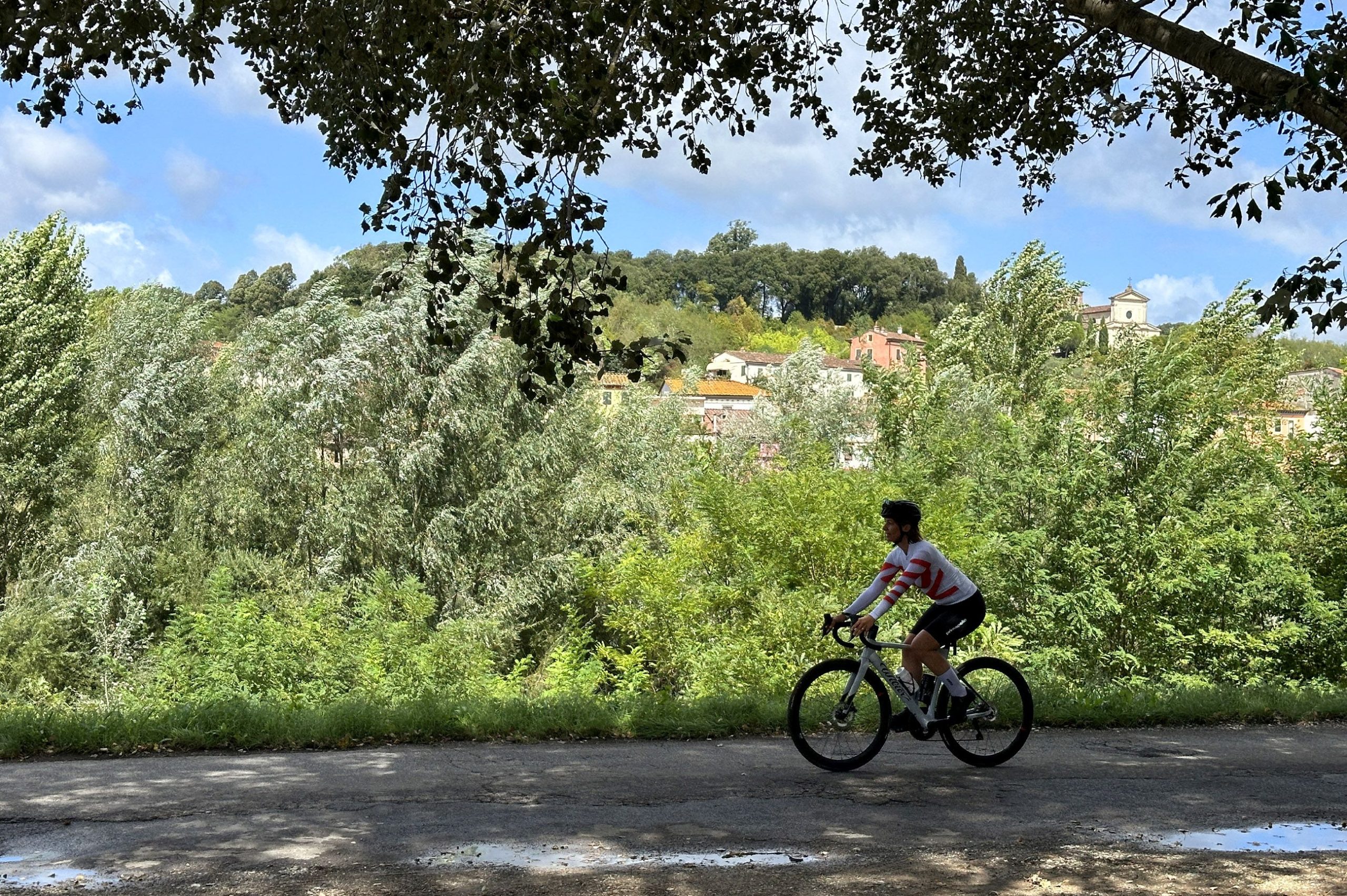 una ragazza in bicicletta pedala su un sentiero in mezzo alla vegetazione. in lontananza c'è una chiesa e alcune case