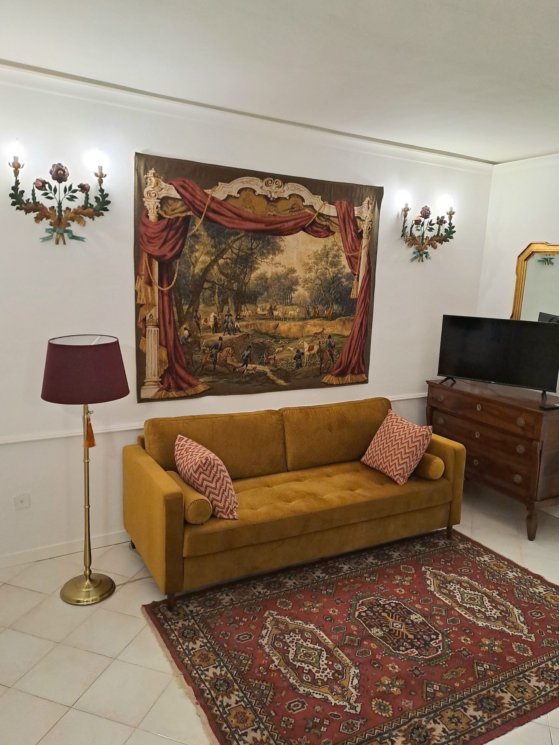 il soggiorno della casa per vacanze Serenità San Martino, arredato in stile classico, con diveno, lampada a terra, un cassettone in legno e un quadro con un paesaggio agreste, senza rinunciare a un grande televisore