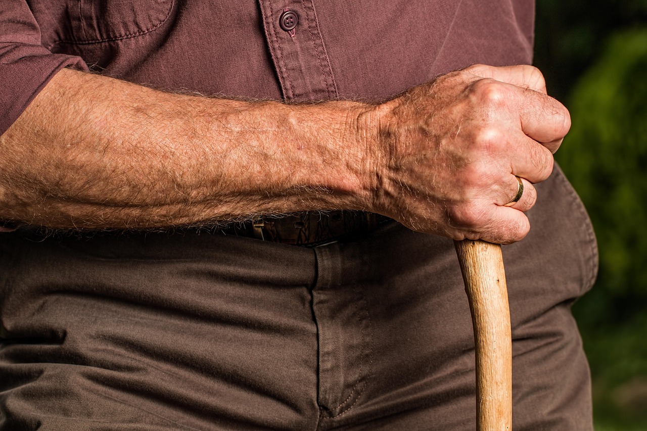 primo piano della mano di un uomo anziano che impugna un bastone da passeggio. Ha un fede al dito.