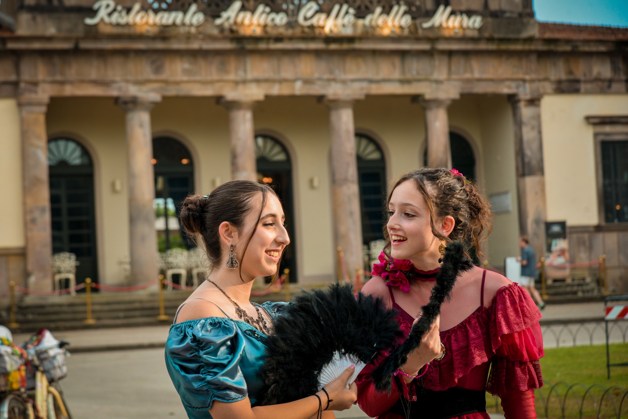 primo piano didue ragazze in abiti primo ottocento che parlano davanti all'edificio del caffè delle Mura